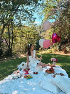 a woman sitting on a blanket in the grass with food and balloons floating above her