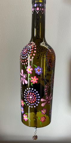 a glass bottle with flowers painted on it hanging from a hook in front of a wall