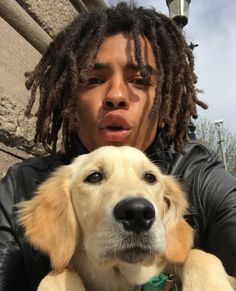 a man with dreadlocks holding a dog in front of his face and looking at the camera