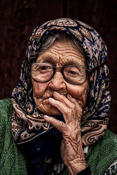 an old woman with glasses and a scarf on her head is looking at the camera