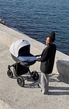 a woman standing next to a baby stroller on the side of a riverbank