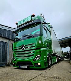 a green semi truck parked in front of a building