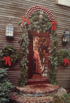 a house decorated for christmas with wreaths on the front door and red bows tied to it