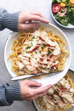 two hands holding a plate of pasta with chicken and parmesan cheese on top