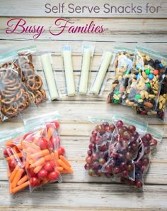 several bags of fruit and snacks on a wooden table, including pretzels, carrots, apples, raisins, and cookies