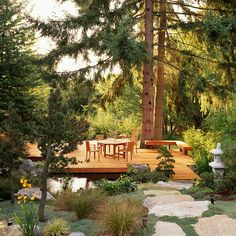 a table and chairs on a wooden deck in the middle of a garden with trees