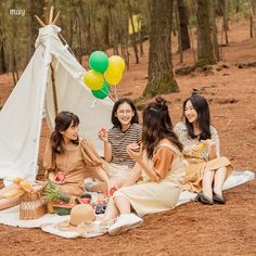 four women sitting on the ground in front of a teepee with food and balloons