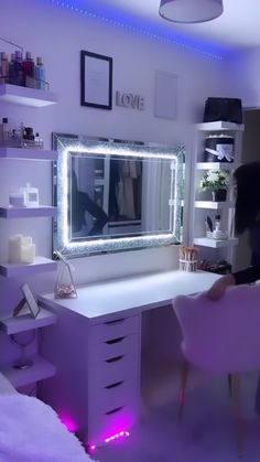 a woman sitting at a desk in front of a large mirror with lights on it