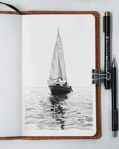 an open notebook with a drawing of a sailboat on the water and two pens next to it