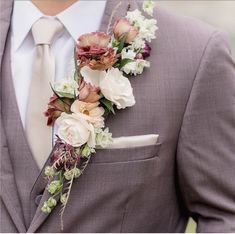 a man in a gray suit with flowers on his lapel and white shirt is wearing a flower boutonniere