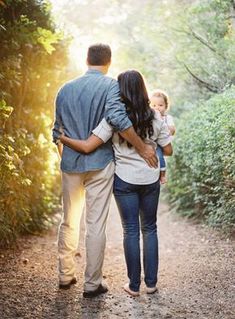 a man, woman and child walking down a dirt path in the woods at sunset