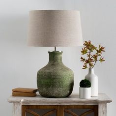 a green vase sitting on top of a wooden table next to a lamp and book