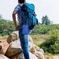 a man with a blue backpack is standing on some rocks and looking at something in the distance