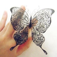 a person's hand holding a black and white butterfly with intricate lace on it