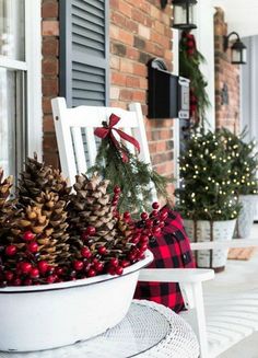 a white chair sitting on top of a porch covered in pine cones and red berries