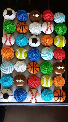 cupcakes decorated with sports balls and basketballs are displayed in a box on a table