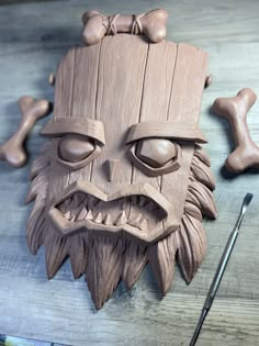 a wooden mask sitting on top of a table next to a pair of paintbrushes