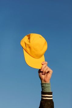 a person holding up a yellow hat in the air with a blue sky behind them