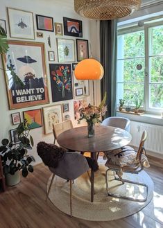 a dining room table surrounded by chairs in front of a window with pictures on the wall