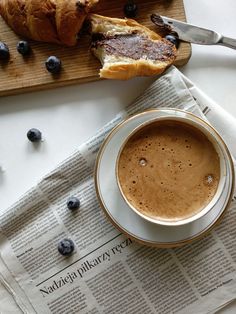 a cup of coffee sitting on top of a newspaper next to a loaf of bread