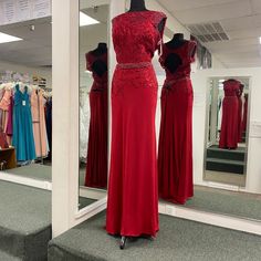 two red dresses are on display in front of a mirror, and one is wearing a beaded belt