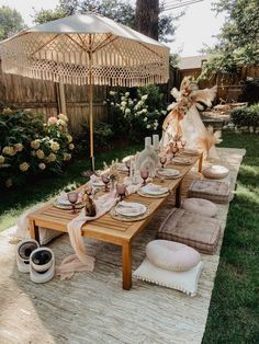 an outdoor table set with plates and place settings under an umbrella in the back yard