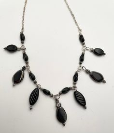 Black, Dark Gray and Silver Necklace and Earrings This necklace is a great basic look, with drops of black.  The drops and beads are all glass.  Along the chain, black slightly twisted glass beads are interspersed.   The drops are all elongated, tear shaped.  The largest are edged in shiny dark silver.  There are also small slightly twisted drops dangling, the same as the black beads interspersed along the chain.  There are medium sized black drops with carving on the sides and larger pressed bl Black Wire Wrapped Necklace For Party, Black Metal Dangle Necklaces, Black Metal Dangle Necklace, Black Teardrop Metal Necklace, Black Metal Teardrop Necklace, Black Beaded Dangle Jewelry, Black Beaded Dangle Necklace, Black Beaded Chain Dangle Jewelry, Elegant Black Necklace With Dangling Beads