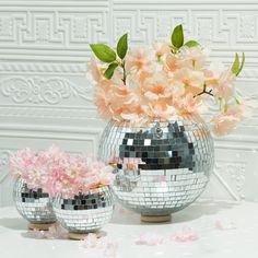 three silver disco ball vases with pink flowers in them sitting on a white table