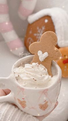 a person holding a cup with whipped cream and a gingerbread man in the mug