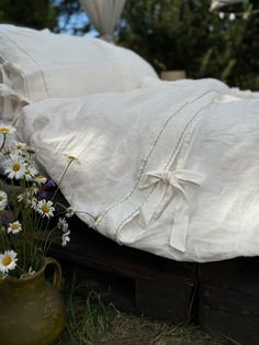 a bed with white linens and daisies on the ground