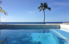 an empty swimming pool with palm trees in the foreground and ocean in the background