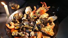 a pan filled with clams and shrimp on top of a table next to a candle