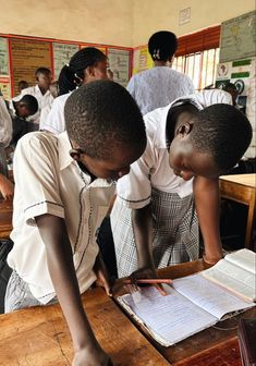 two children are writing on a piece of paper at a desk in a class room