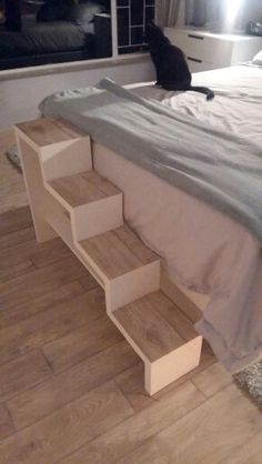 a cat sitting on top of a bed next to a window in a room with wooden floors