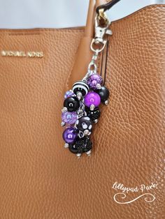 a handbag is adorned with purple and black beaded charms, which are hanging from a metal chain