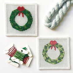 three cross stitch christmas coasters on a white surface with twine and scissors next to them