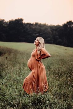 a pregnant woman in an orange dress is standing in the middle of a grassy field