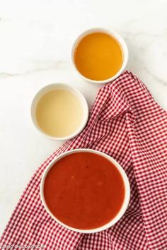 three bowls of soup are sitting on a red and white checkered cloth next to each other