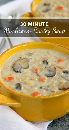 two yellow bowls filled with mushroom barley soup on top of a white table cloth next to silver spoons