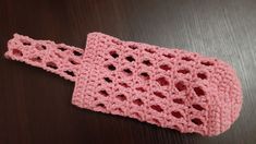 a pink crocheted headband laying on top of a wooden table next to a black surface