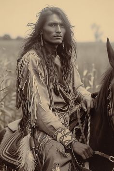 an old photo of a native american man on a horse in a field with tall grass