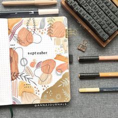 an open planner with pencils, markers and other items around it on a table