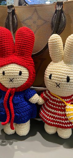 two crocheted stuffed animals sitting next to each other in front of a purse