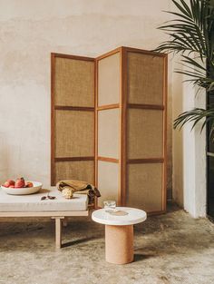 a room divider sitting next to a table with fruit on it and a plant in the corner