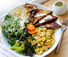 a white plate topped with lots of food next to a fork and cup on top of a table