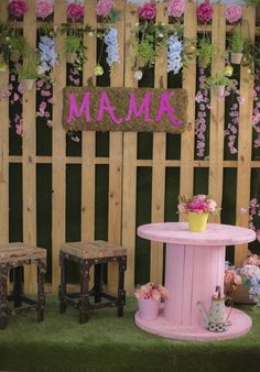 a pink table and two stools in front of a wooden fence with flowers on it