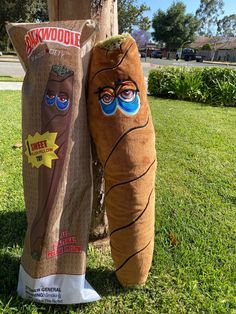 two stuffed animals standing next to each other in the grass near a wooden pole with an advertisement on it