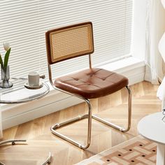 a brown chair sitting in front of a window next to a white vase with flowers