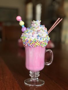 a pink drink with sprinkles and candy in it on a wooden table