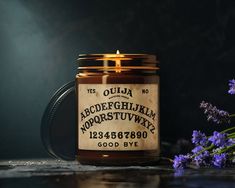 a jar of ouja alphabet and numbers candle next to some purple flowers on a table